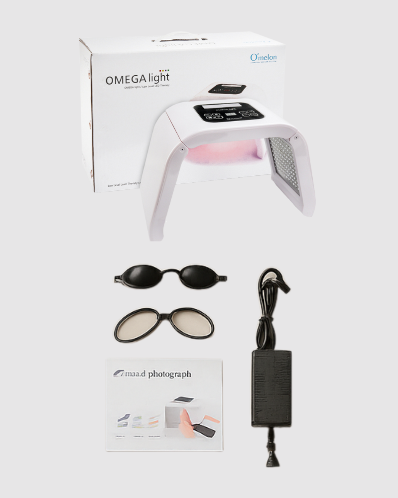 Omega Light device with packaging, goggles, and power adapter on a beige background