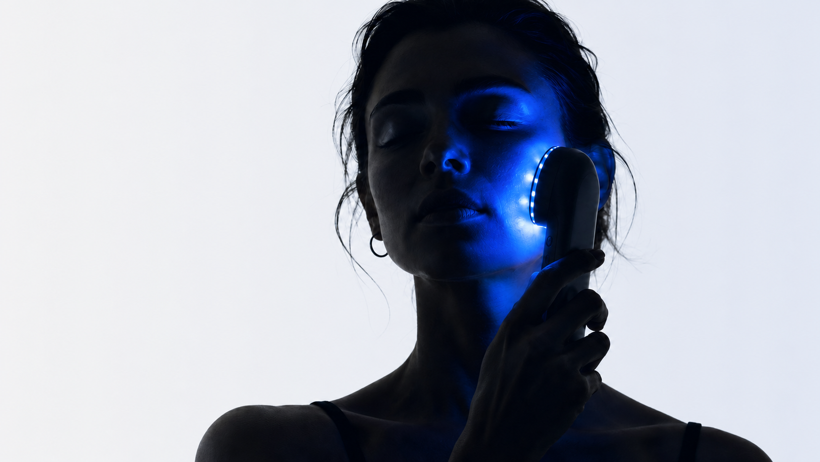 Woman using a blue LED light therapy device on her cheek for clearer-looking skin.