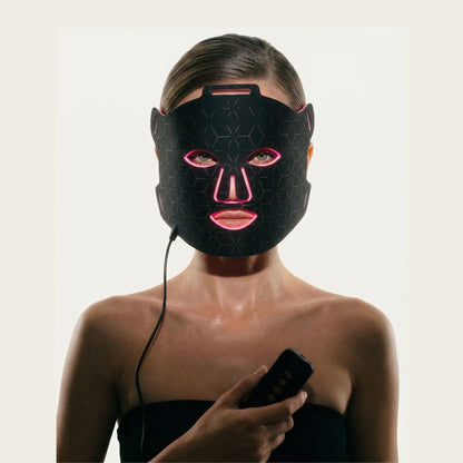 Woman wearing Luminmax LED red light therapy face mask and holding controller