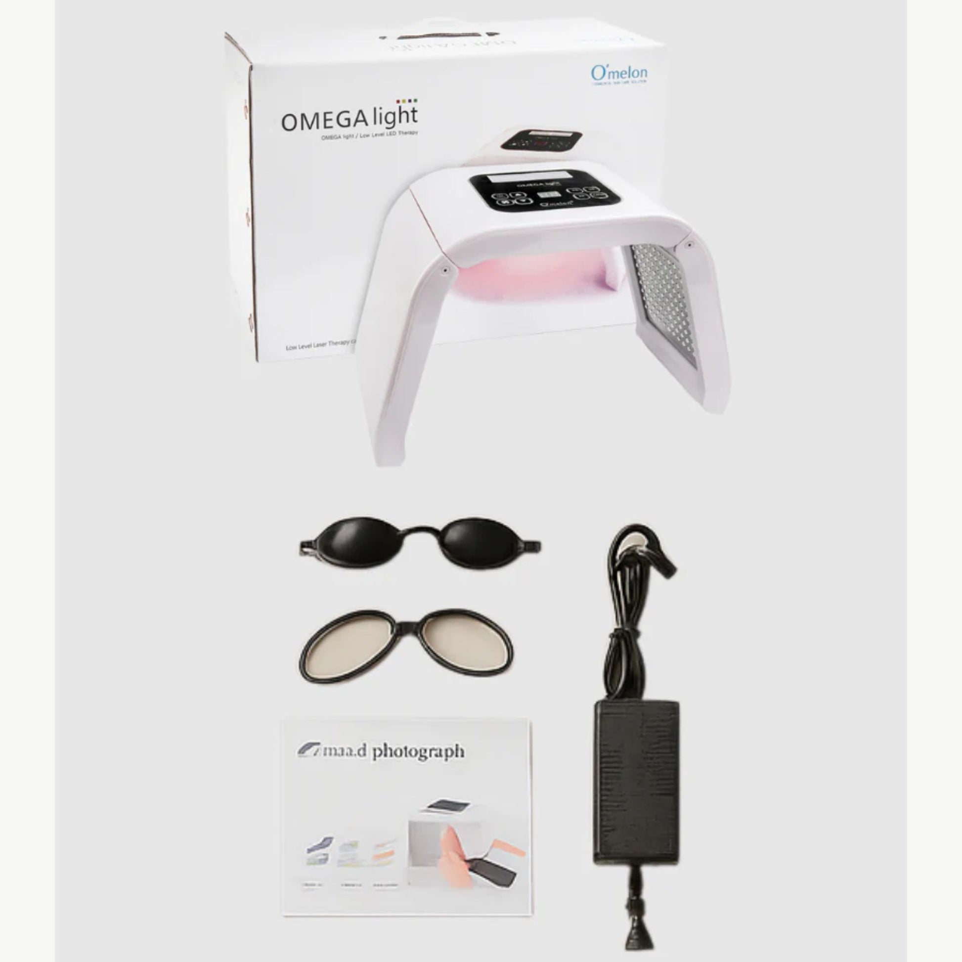 Omega Light device with packaging, goggles, and power adapter on a beige background